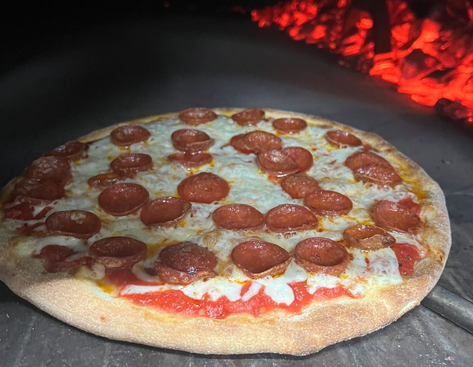 Pepperoni pizza cooking with glowing red coals nearby.